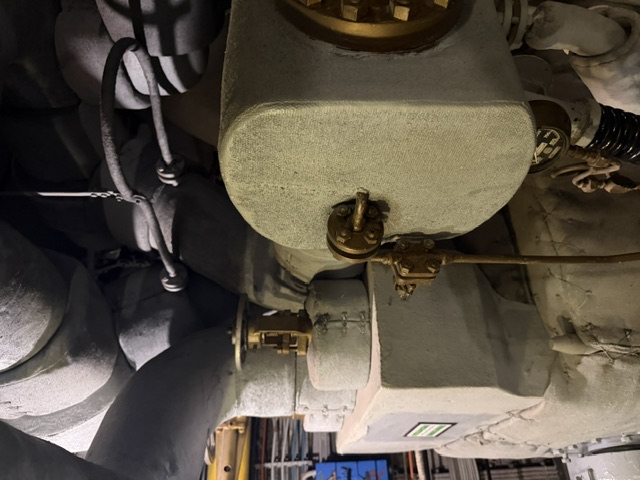 Thick thermal lagging (insulation) covers the steam piping, valve bonnets, and a large valve body in a machinery space aboard USS Alabama, with bronze valve stems and fittings protruding through the insulation.