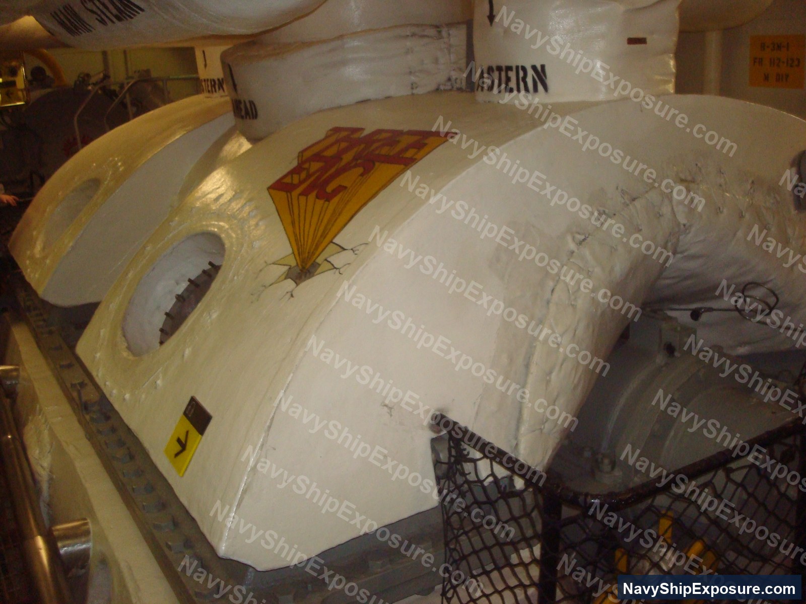 Interior view of a large cylindrical boiler or pressure vessel in USS Midway's machinery space, with visible lagging/insulation material and industrial piping and equipment.