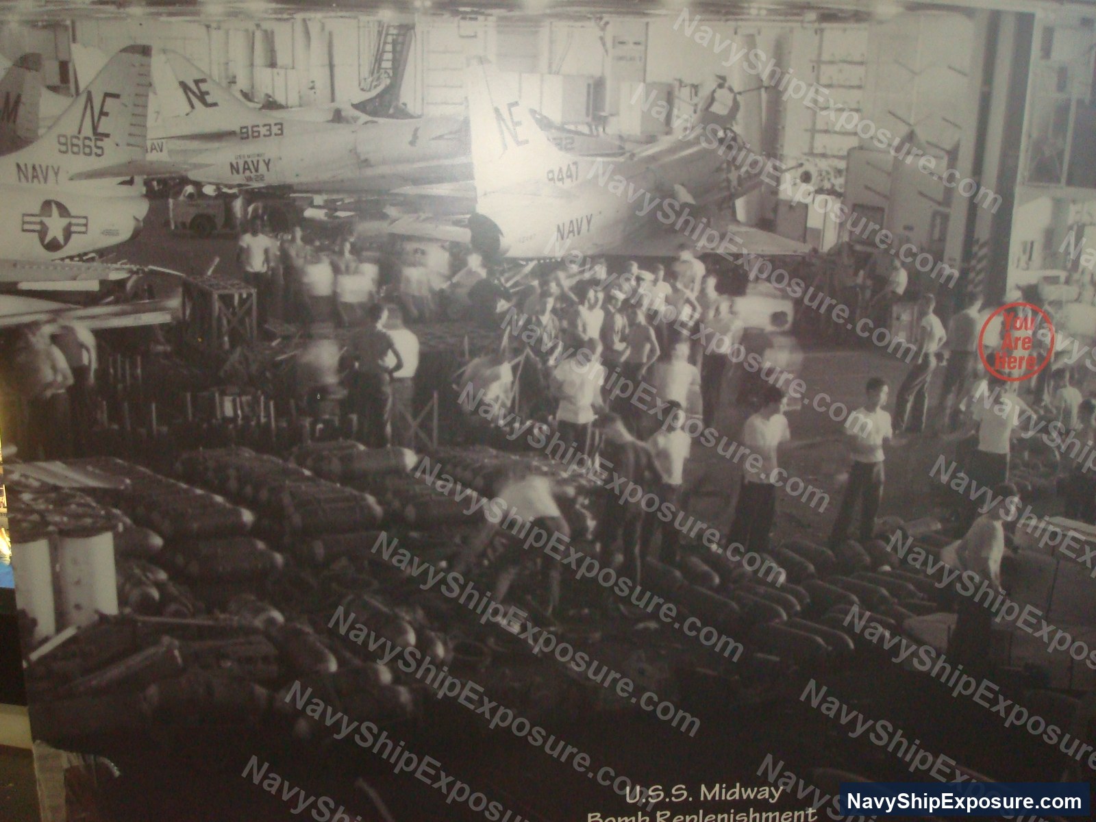 Interior view of USS Midway's bomb replenishment area showing naval personnel working with ordnance and aircraft in the hangar bay during the carrier's operational period.