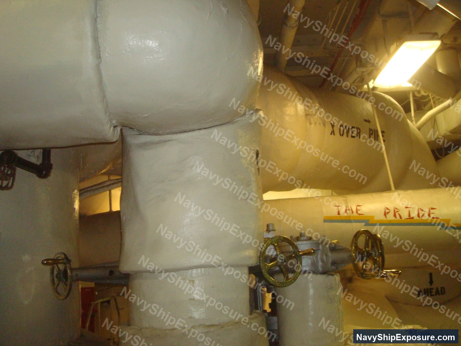 Engine room or machinery space aboard USS Midway showing large cylindrical equipment with hand wheels, piping, insulation wrapping, and industrial naval machinery typical of a 1940s-era aircraft carrier's propulsion systems.