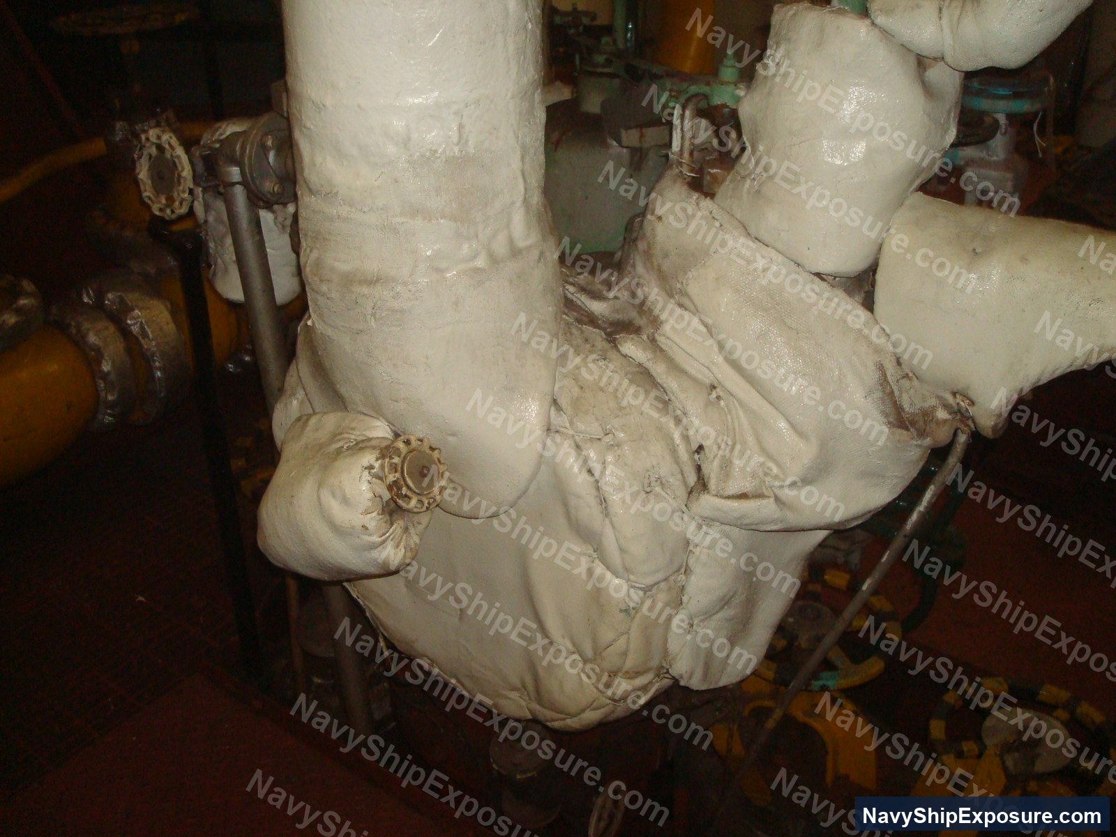 Insulated pipe work in an engine room or machinery space of USS Midway, showing deteriorated asbestos thermal insulation wrapping on large diameter piping and elbow joints.