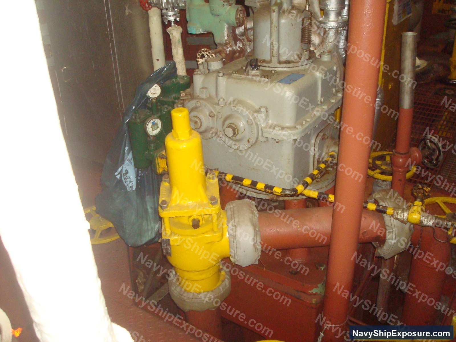 Engine room or machinery space aboard USS Midway showing industrial pump equipment with yellow safety device, red piping, and cream-colored machinery typical of 1940s-1950s naval vessel propulsion systems.