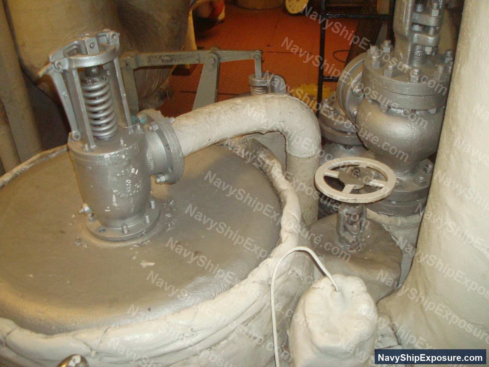 Engine room or machinery space piping assembly with insulated pipes, valves, and mechanical equipment typical of USS Midway's steam propulsion system, showing deteriorated thermal insulation consistent with asbestos-containing materials used on naval vessels of that era.