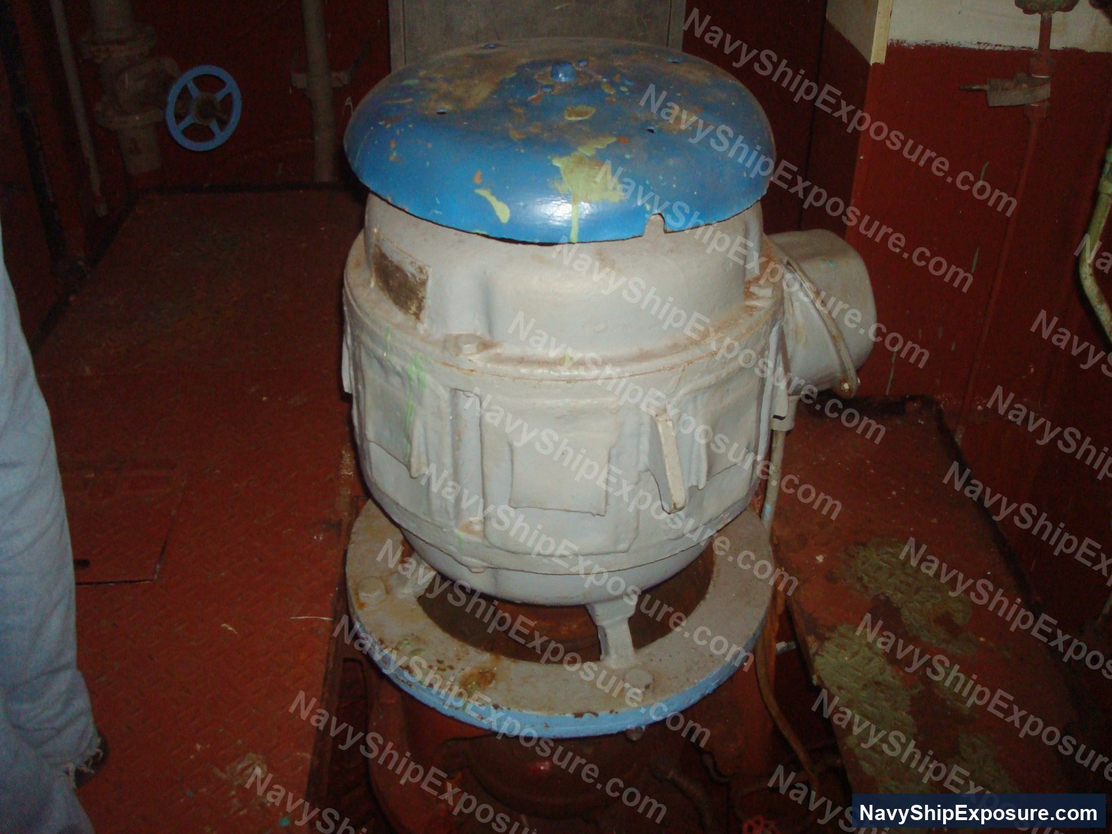 An electric motor with a blue top mounted on a base in an engine room or machinery space of USS Midway, showing deteriorated condition and potential asbestos-containing insulation materials typical of 1940s-era naval vessels.