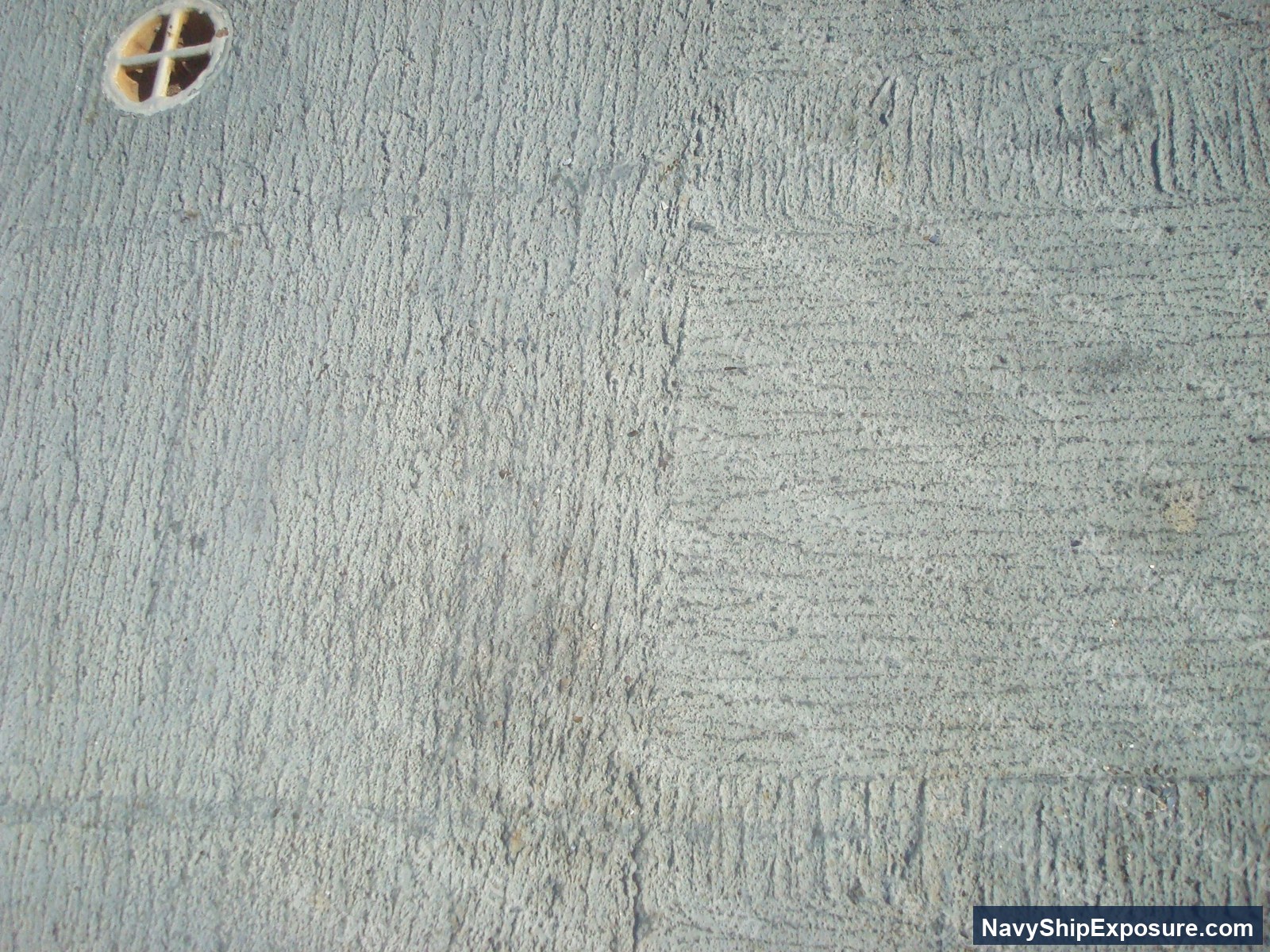 Interior surface of a ship machinery or engineering space showing textured insulation material with visible wear patterns and a circular ventilation or access port with a cross-pattern grate.