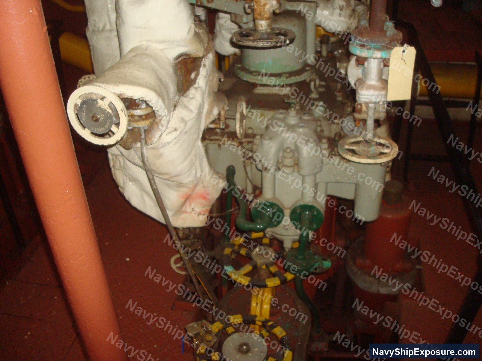 Engine room or machinery space from USS Midway showing insulated piping, valves, and industrial equipment typical of 1940s-1950s naval steam propulsion systems.