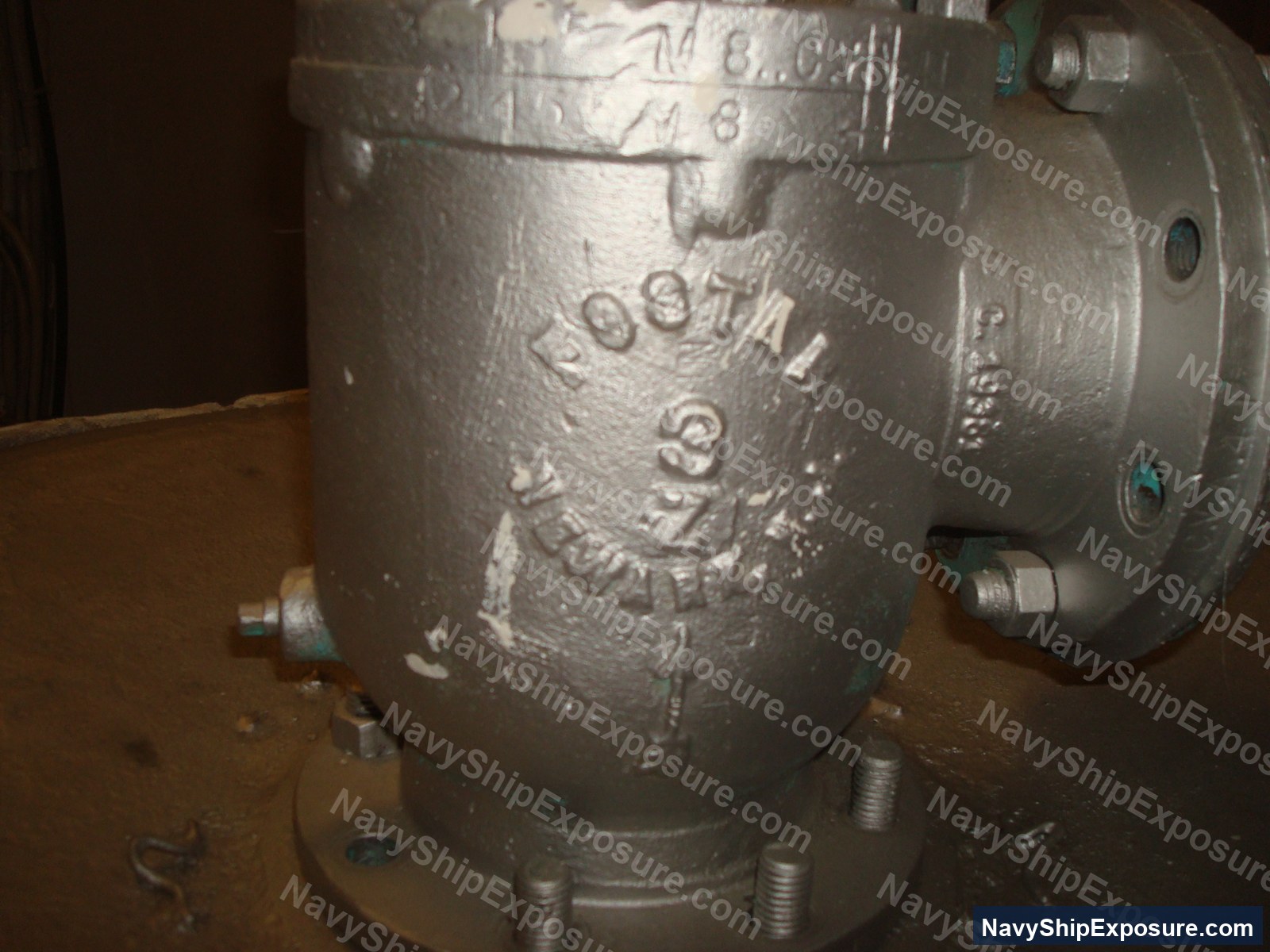 Close-up photograph of an industrial pump or compressor unit with cast metal housing and visible serial number marking, typical of machinery found in naval vessel engine rooms.
