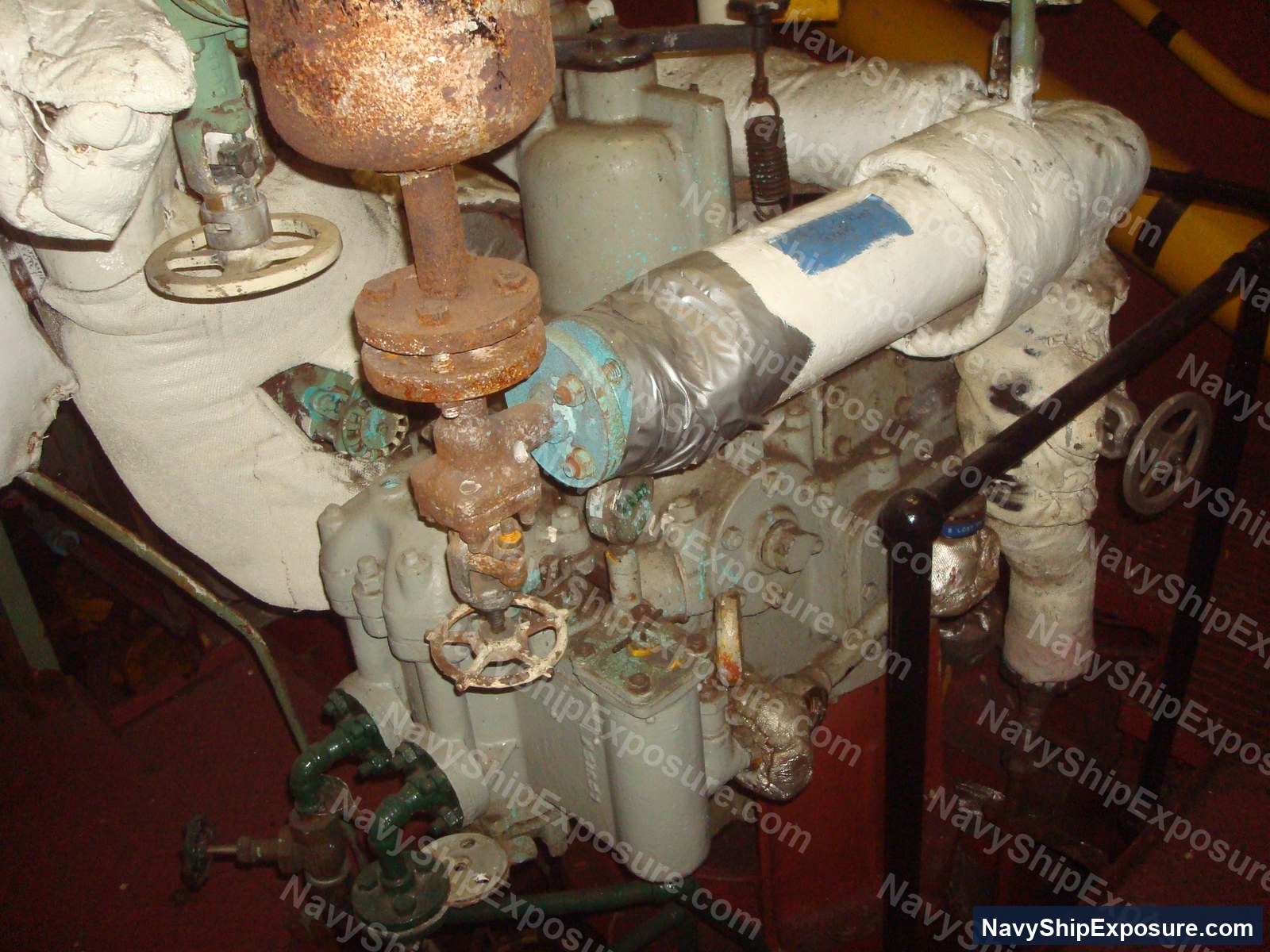 Engine room or machinery space equipment from USS Midway showing deteriorated piping, insulation wrapping, valves, and corroded metal components typical of naval propulsion systems that historically contained asbestos materials.